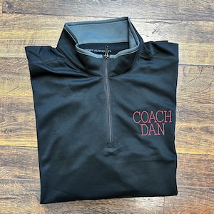 May include: Black quarter-zip pullover with a gray collar and a red embroidered logo that says "COACH DAN".