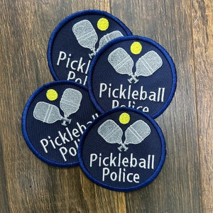 May include: Four blue and white embroidered patches with the text "Pickleball Police" and a graphic of two pickleball paddles and a yellow ball.