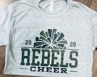 May include: A heather gray short-sleeve t-shirt featuring a dark green graphic of a pom-pom above the text 20 REBELS 26 and the word CHEER. The design includes horizontal lines separating the elements, and a white brand label is at the neck.
