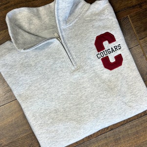 May include: Grey quarter-zip sweatshirt with a red embroidered letter "C" and the word "COUGARS" in black lettering.