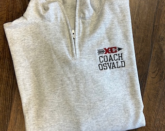 May include: Gray quarter-zip sweatshirt with a black embroidered logo that says "XC COACH OSVALD" with a red arrow and an "X" in the middle.