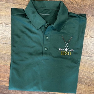 Op de afbeelding: Donkergroene poloshirt met een sluiting met drie knopen en een kraag. De shirt heeft een geborduurd golf-thema ontwerp met gekruiste golfclubs, een golfbal en de letters "HSO" in geel.