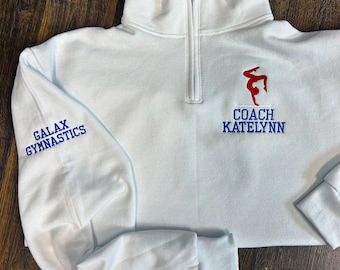 May include: White quarter-zip sweatshirt with blue embroidery on the sleeve that says "Galax Gymnastics" and blue embroidery on the front that says "Coach Katelyn" with a red and blue gymnast silhouette.