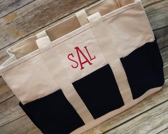 May include: A two-tone canvas tote bag featuring a cream-colored upper section and a black lower section. The bag includes two cream-colored fabric handles and is personalized with the embroidered red monogram letters SAL on the front panel.
