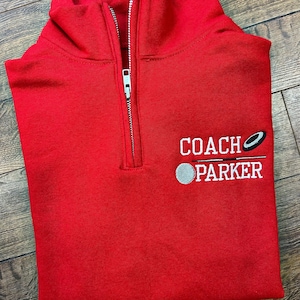 Op de afbeelding: Rood quarter-zip sweatshirt met witte geborduurde tekst "COACH PARKER" en een hockey puck-afbeelding.