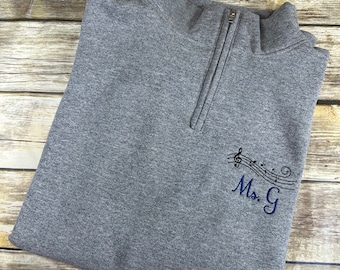 May include: Gray quarter-zip sweatshirt with a black embroidered design of musical notes and the text "Ms. G"