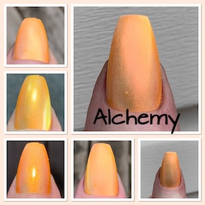May include: Close-up of a fingernail painted with orange nail polish. The word "Alchemy" is written in black script on the nail. The polish has a matte finish and appears to have a slight shimmer.