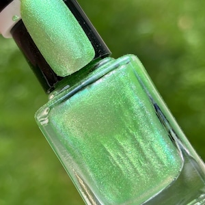 May include: A bottle of green nail polish with a shimmery finish. The bottle is clear glass and has a black cap.