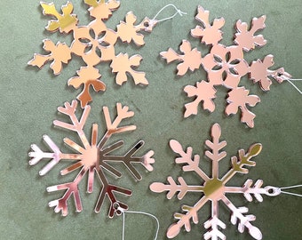 May include: Four rose gold snowflake ornaments with white string hangers. The snowflakes are all different designs.