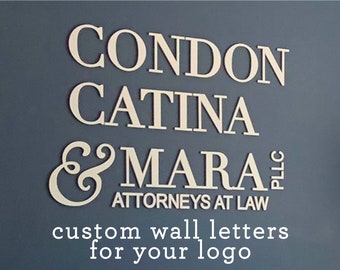 May include: White custom wall letters spelling "Condon Catina & Mara, PLLC, Attorneys at Law" on a blue wall. The text "custom wall letters for your logo" is below the name.