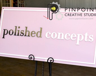May include: Pink sign with white border and the words "polished concepts" in silver and white lettering. The sign also includes the text "Pinpoint Creative Studio" and a website address.