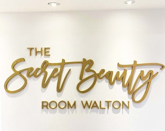 May include: Gold lettering on a white wall reads "The Secret Beauty Room Walton".