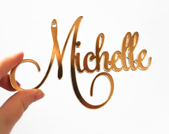 May include: Gold mirror acrylic name sign with the name "Michelle" in a cursive font.