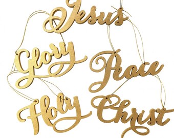 May include: Gold-colored wooden Christmas ornaments with the words "Jesus", "Glory", "Peace", "Holy", and "Christ" in a cursive font. Each ornament is suspended by a thin gold string, perfect for holiday decorating.