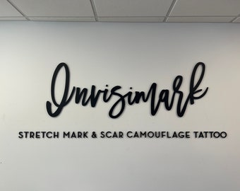 May include: A white wall with a black sign that reads "Invisimark Stretch Mark & Scar Camouflage Tattoo". The word "Invisimark" is written in a large, stylized font.