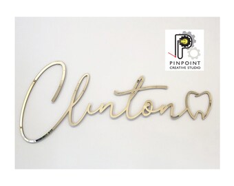 May include: Gold-colored, cursive-style sign that spells out "Clinton" with a tooth-shaped design at the end. The sign is likely for a dental practice. The Pinpoint Creative Studio logo is in the upper right corner.