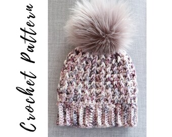 Op de afbeelding: Een gebreide beanie met een pluche pompon in tinten roze, wit en grijs. De beanie heeft een textuurpatroon.