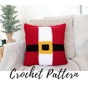 May include: Crochet pattern for a Santa Claus pillow. The pillow is red and white with a black belt and a gold buckle. The pillow is sitting on a white couch.