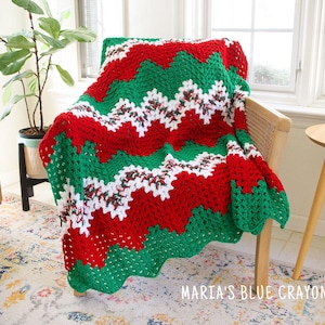 May include: A crocheted blanket featuring a chevron pattern in alternating stripes of solid red, solid green, and a variegated white, red, and green yarn. The text "MARIA'S BLUE CRAYON" is printed in white in the bottom right corner.