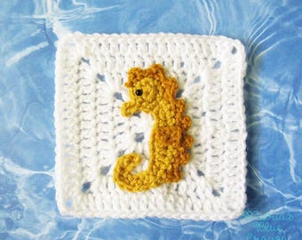 May include: A white crocheted square with a yellow and orange seahorse applique. The seahorse has a black eye and is centered on the square. The background is a blue water pattern.