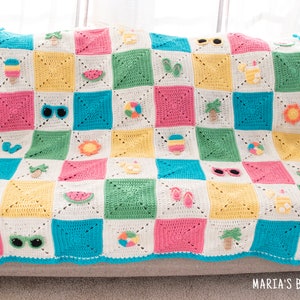 May include: A colourful crocheted blanket with a summer theme. The blanket is made up of squares with different summer-themed motifs, including ice cream cones, sunglasses, watermelons, palm trees, and beach balls. The blanket is on a light grey sofa.
