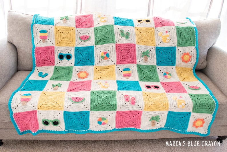 May include: A colourful crocheted blanket with a summer theme. The blanket is made up of squares with different summer-themed motifs, including ice cream cones, sunglasses, watermelons, palm trees, and beach balls. The blanket is on a light grey sofa.