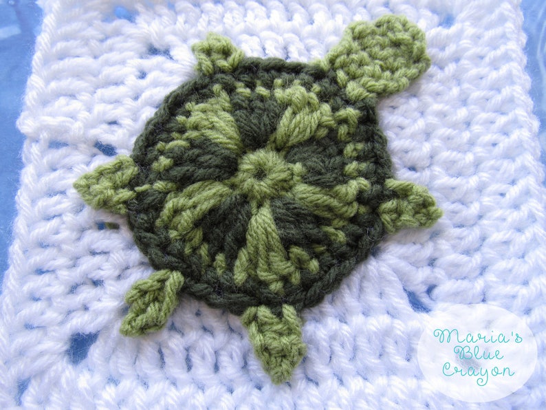 May include: A crocheted turtle applique in shades of green, with a white crocheted background. The turtle is a flat applique, with a detailed shell and four legs.