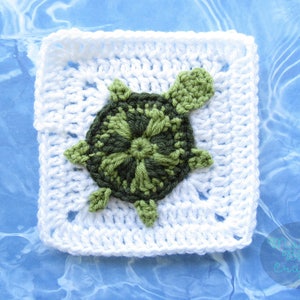 May include: A white crocheted square with a green crocheted turtle in the center. The turtle has a detailed shell and a simple head and legs.