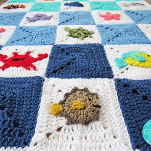 May include: A crocheted baby blanket with a blue, white, and turquoise checkered pattern. The blanket features various sea creatures, including a crab, a fish, a starfish, and an octopus.