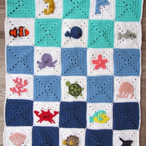 May include: A crocheted baby blanket with a sea life theme. The blanket is made up of squares with different sea creatures, including a seahorse, whale, octopus, turtle, crab, and fish. The blanket is in shades of blue, green, white, red, and orange.
