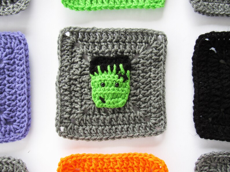 May include: A gray crochet square with a green Frankenstein face in the center. The square is surrounded by other squares in different colors, including purple, green, black, orange, and gray.
