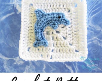 May include: A square white crochet granny square featuring a light blue crocheted dolphin appliqué in the center. The dolphin has a small black bead for an eye. The text "Maria's Blue Crayon" is visible in the bottom right corner of the square.