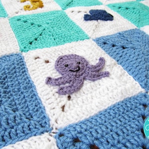 May include: A crocheted baby blanket with a blue, white, and turquoise color scheme. The blanket features a variety of sea creatures, including an octopus, a seahorse, and a fish. The blanket is made with a soft, textured yarn.