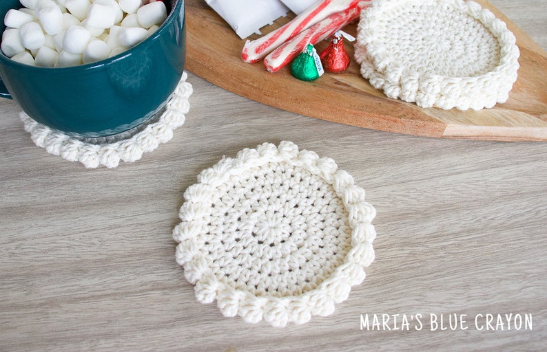 May include: Three white crocheted coasters with a raised edge. The coasters are on a wooden surface.