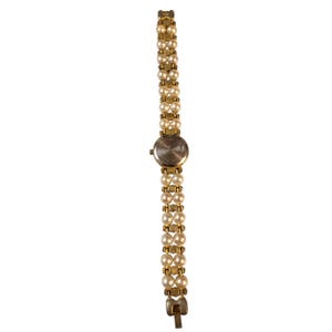 May include: A gold-toned wristwatch with a band composed of two rows of faux pearls. The watch face is round with a silver-colored finish. The band is connected with gold-toned metal links. The watch is a classic, elegant accessory.