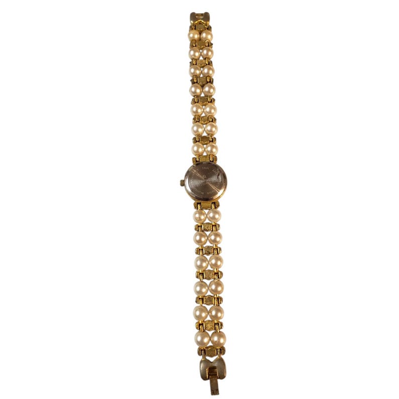 May include: A gold-toned wristwatch with a band composed of two rows of faux pearls. The watch face is round with a silver-colored finish. The band is connected with gold-toned metal links. The watch is a classic, elegant accessory.