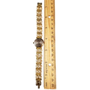 May include: A vintage gold-toned watch with a pearl bracelet band. The watch face is round with a silver-colored dial. The band is made of small, round, cream-colored pearls. The watch is approximately 7 inches long.