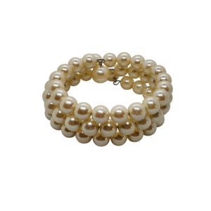 May include: A multi-strand wrap bracelet composed of three rows of cream-colored, spherical faux pearls. The design features a flexible, coiled structure that allows for easy wrapping around the wrist, with a single pearl dangling from a metal loop.