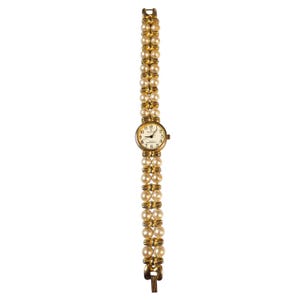 May include: A gold-toned wristwatch with a cream-colored face and a double-strand pearl band. The watch face features black numerals and hands, with the brand name "Relic" printed below the 12 o'clock marker. The band is approximately 7 inches long.