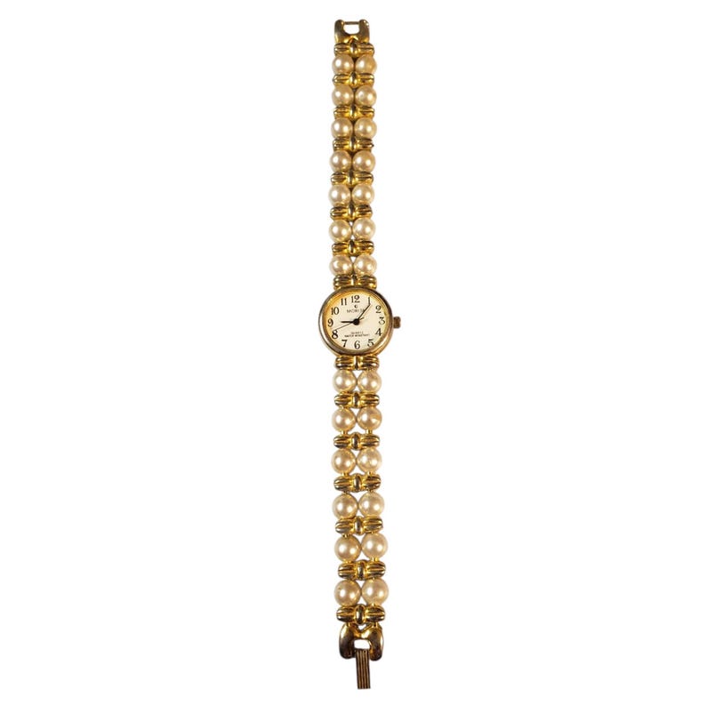 May include: A gold-toned wristwatch with a cream-colored face and a double-strand pearl band. The watch face features black numerals and hands, with the brand name "Relic" printed below the 12 o'clock marker. The band is approximately 7 inches long.