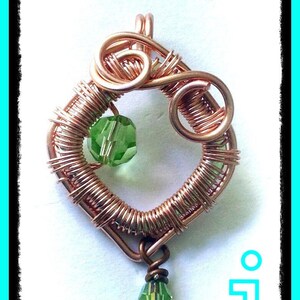 May include: A copper wire pendant with a green glass bead in the centre and a smaller green glass bead dangling from the bottom.