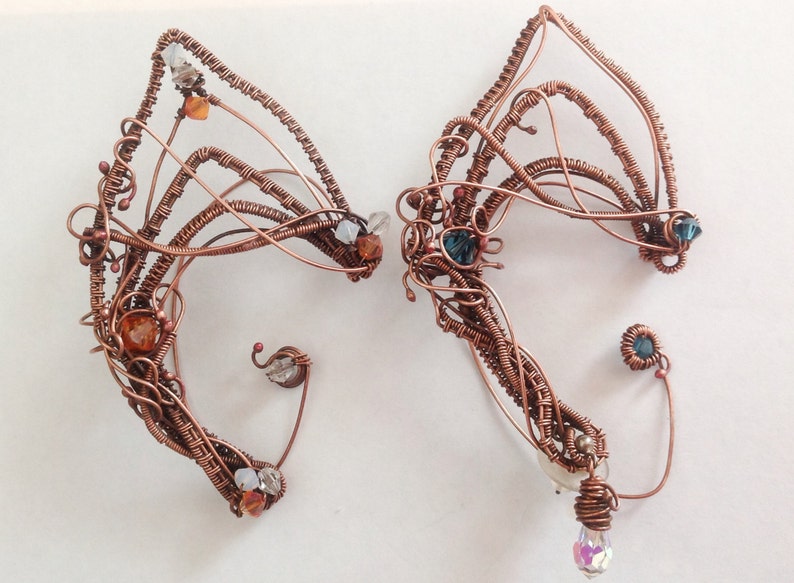 May include: A pair of copper wire ear cuffs featuring a variety of coloured beads and crystals. The ear cuffs are intricately designed with a delicate, organic shape.