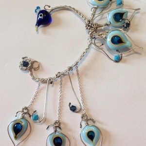 May include: Silver ear cuff with blue and white glass beads in the shape of eyes. The cuff has three dangling charms with blue and white glass beads in the shape of eyes.