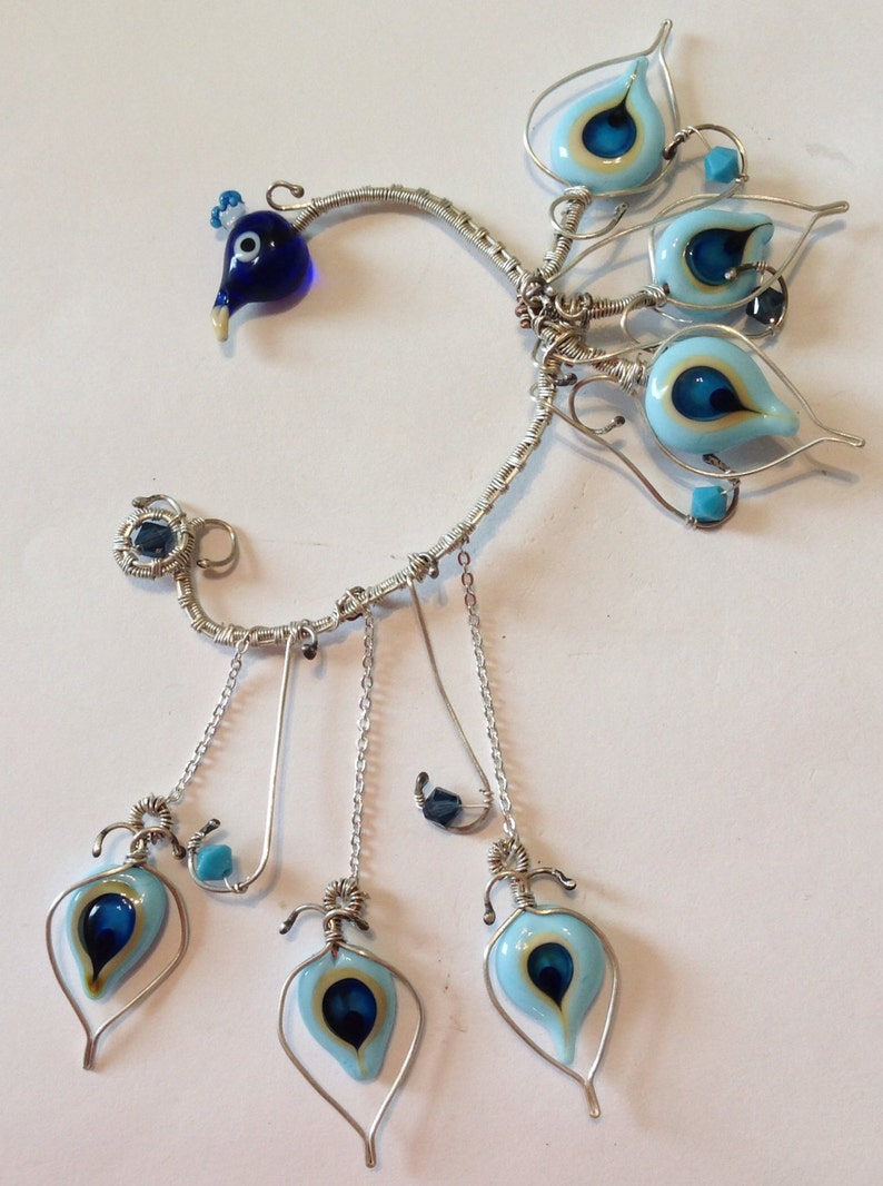 Pu&ograve; includere: Orecchino d'argento con perline di vetro blu e bianche a forma di occhi. L'orecchino ha tre ciondoli pendenti con perline di vetro blu e bianche a forma di occhi.