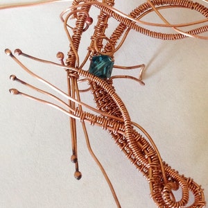 May include: A copper wire sculpture of a dragonfly with a teal blue gemstone in the centre.
