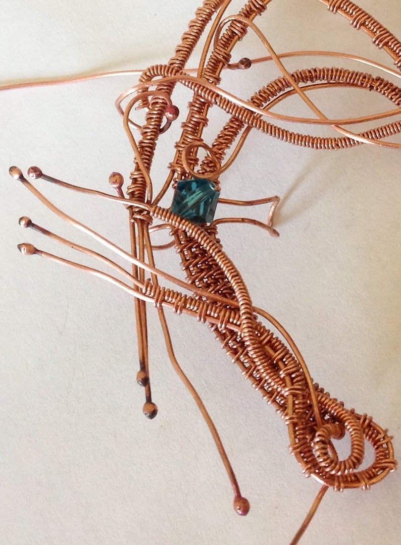 May include: A copper wire sculpture of a dragonfly with a teal blue gemstone in the centre.