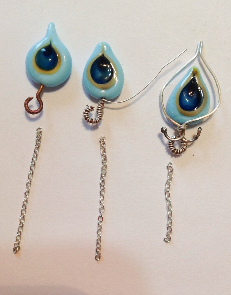 Pu&ograve; includere: Tre paia di orecchini con perline di vetro blu e oro a forma di occhio di pavone. Due paia hanno un semplice anello di filo e il terzo paio ha un design di filo pi&ugrave; elaborato.