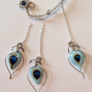 Pu&ograve; includere: Tre ciondoli avvolti in filo d'argento con forme a goccia di vetro blu e oro. Ogni ciondolo &egrave; appeso a una catena d'argento.