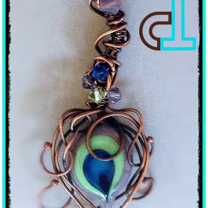 May include: A copper wire wrapped pendant featuring a blue, green and purple glass eye design. The pendant is decorated with small blue, green and purple glass beads.