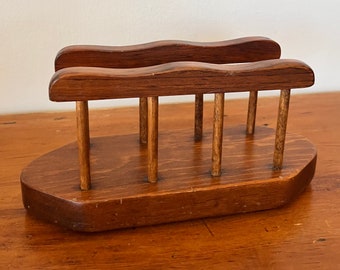 May include: A wooden napkin holder with a natural brown finish. The holder has two curved top rails and a rectangular base.